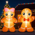 Gingerbread girl with a pink bow and gingerbread boy with a red bow tie inflatables glowing at night