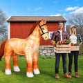 Realistic brown horse inflatable in front of a red barn beside a couple holding produce