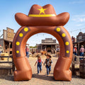 Brown horseshoe arch inflatable topped with a cowgirl hat at a western town with kids walking through