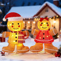Lighted gingerbread boy in a Santa hat and girl in a red dress standing in the snow