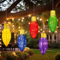 Five large lighted Christmas bulb ornaments in bright colors hanging from a tree at night