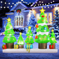 Row of cartoon Christmas tree inflatables with stars and gifts on a snowy base in front of a lit house