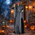 Life-size hooded grim reaper prop with red eyes in tattered robes among pumpkins at night